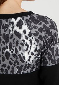 Primo piano della parte superiore della schiena di una persona che indossa un top con stampa leopardata nero e grigia e un collo a collare nero.