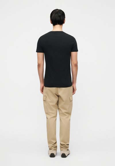 Μαύρο βαμβακερό μπλουζάκι με κοντά μανίκια και στρογγυλή λαιμόκοψη, σε συνδυασμό με μπεζ cargo παντελόνι με πλαϊνές τσέπες και ίσια μπατζάκια.
