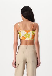 Top floreale corto con design bianco, verde e arancione, spalline sottili e dorso quadrato, abbinato a pantaloni cargo beige.