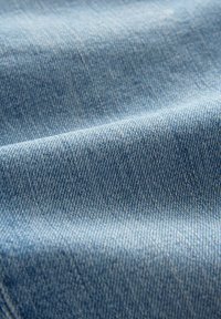 Vaatekangas vaaleansinisestä denimistä, jossa on hienovarainen tekstuuri ja vino kudontamalli. Pinta on sileä, mutta siinä on pieniä vaihteluita.