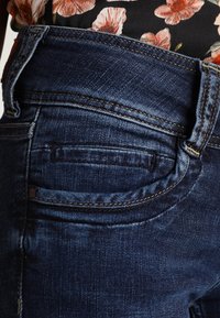 Granatowe dżinsy o klasycznym kroju, z wyraźnym przeszyciem oraz tylną kieszenią z ozdobnym guzikiem.