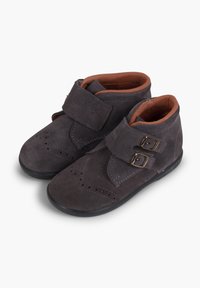 Botas de ante gris oscuro hasta el tobillo con correas de doble hebilla, detalles de brogue y un interior marrón contrastante. Suela plana de goma.