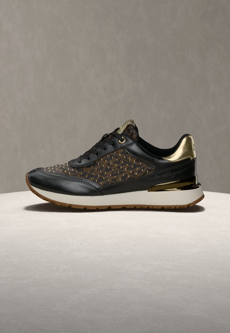 Chaussure de sport noire avec des accents dorés, empeigne texturée avec des détails cloutés et un talon doré brillant. Semelle intermédiaire blanche et semelle extérieure en caoutchouc.