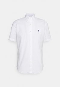 Vit kortärmad skjorta med knappar, tillverkad av vävt tyg, med klassisk krage och en liten marinblå logo på vänster bröst.