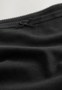 Czarna tkanina o gładkiej fakturze, zdobiona delikatną koronkową lamówką i małą kokardką na górnej krawędzi.