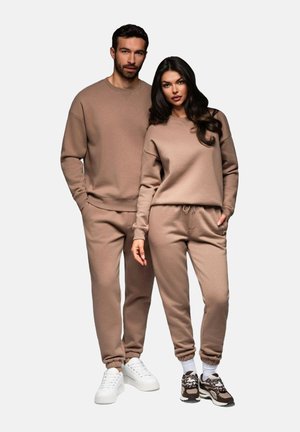 Zwei Modelle tragen passende braune Sweatshirts und Jogginghosen aus einem kuscheligen Stoff. Das Sweatshirt hat einen Rundhalsausschnitt; die Jogginghosen verfügen über einen elastischen Bund.