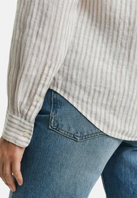 Gestreepte linnen overhemd met beige en witte verticale strepen, met een knoopmanchet, gecombineerd met blauwe denim jeans met een achterzaknaaddetail.