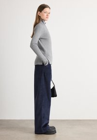 Grauer Rippenpullover mit hohem Kragen, navyblaue Cord-Hosen mit weitem Bein, schwarze Plattformschuhe und kleine schwarze Handtasche.