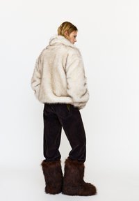 Műszőrme krémszínű kabát, túlméretezett fazon, puha tapintású. Sötétbarna kordnadrág párosítva hozzáillő műszőrme csizmával.