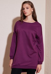 Felpa oversize viola con maniche lunghe, scollatura a barca, polsini e fondo a coste, realizzata in tessuto morbido e liscio. Senza fantasie o dettagli.