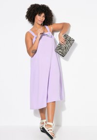 Lavendelfarbenes ärmelloses Kleid aus strukturiertem Stoff, das bis zur Mitte der Waden reicht. Kombiniert mit einer schwarz-weißen Zebra-Print-Clutch und weißen Riemchensandalen.
