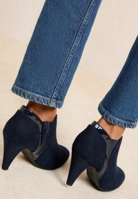 Botines de ante azul marino con acentos de charol, punta afilada y tacón de estilete. Cierre lateral para facilitar el uso. Jeans de mezclilla con dobladillo.
