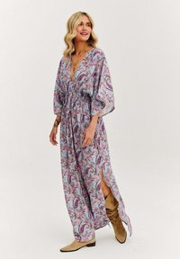 Dlhé, voľné šaty z svetlomodrej látky s paisley vzorom v ružovej a fialovej farbe. Majú hlboký V-krk a sťahovaný pás so bočnými rozparkami.