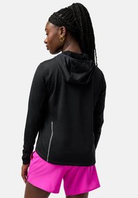 Black zip-up hoodie featuring a textured surface, a hood, and reflective accents, paired with pink athletic shorts.