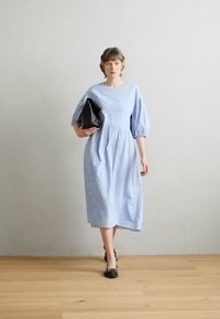 Lyseblå og hvite striper, knelengde kjole med pufferm, tettsittende liv og en rynket skjørt. Svart clutch-veske, flate sko.