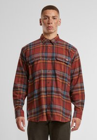 Red and blue plaid flannel shirt with a button-up front, two chest pockets, and a collar. Fabric appears soft with a slightly rough texture.