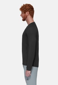 Zwarte langemouwen shirt met ronde hals, gladde textuur en vlakke naden, gedragen door een persoon in lichtgrijze broek.
