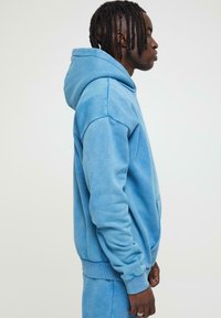 Hoodie bleu clair en tissu doux, doté d'une capuche avec cordon de serrage, de poches latérales et de poignets et ourlet côtelés. Texture lisse, coupe décontractée.