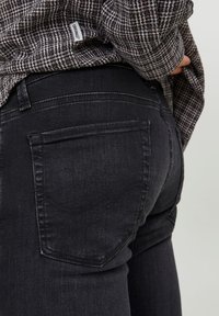 Schwarze Denim-Jeans mit strukturierter Passform, auffälligen Gesäßtaschen und dezenten Nähten. Kombiniert mit einem strukturierten Karo-Top.