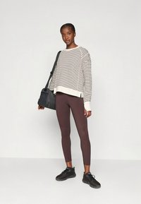 Camisola às riscas creme e preta, corte largo, combinada com leggings castanhas. Usada com sapatos pretos e uma mala escura. Design simples e funcional.