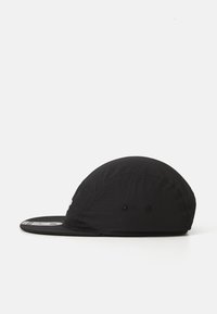 Black lightweight five-panel cap with a flat brim, ventilation eyelets, and a sticker on the brim against a white background.