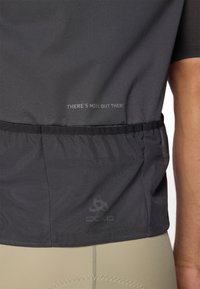 T-shirt de sport à manches courtes, gris foncé avec un tissu texturé. Présente un ourlet inférieur cintré et un texte imprimé : "IL Y A PLUS LOIN." Logo visible.