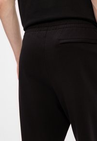 Μαύροι παντελόνια φόρμας με ελαστική μέση, λεία υφή, slim fit και μία μόνο πίσω τσέπη. Απλή σχεδίαση χωρίς ορατά σχέδια.