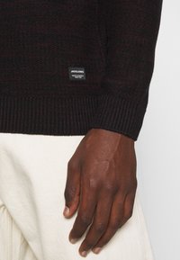Donkerrood en zwart gebreid sweater met geribde manchetten, voorzien van een klein merklabel op de zoom en een gestructureerde stof.