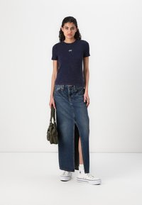 Marineblå T-shirt med korte ærmer og "GAP" logo, parret med en lang denimnederdel med slid foran, og hvide kanvas sneakers.