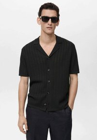 Black short-sleeve shirt with a textured pattern, button-up front, and notched collar, paired with dark sunglasses.