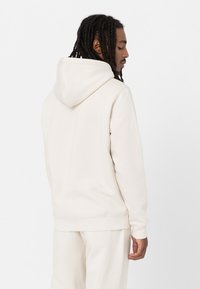 Light beige hoodie made of soft fabric, featuring a drawstring hood, ribbed cuffs, and a relaxed fit, paired with matching pants.