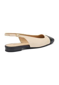 Scarpa slingback in pelle beige con punta tonda nera, caratterizzata da tacco basso e cinturino regolabile per una vestibilità sicura. Texture liscia.