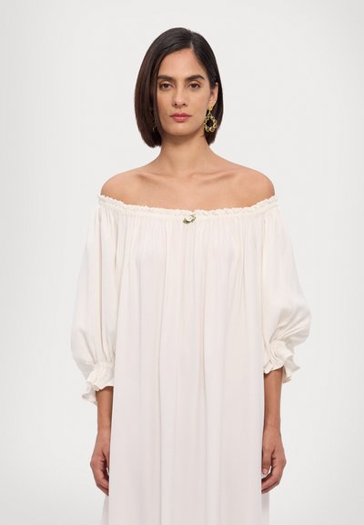 Robe blanche décolletée avec des manches ballon, encolure froncée et un petit accent floral au centre. Tissu lisse et léger.