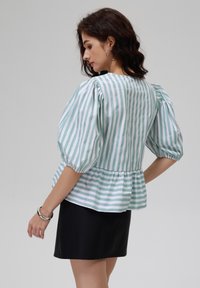 Gestreifte Bluse in Mintgrün und Weiß, mit puffigen Ärmeln, einem Peplum-Saum und einem leichten Stoff. Getragen mit einem schwarzen Rock.