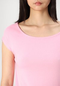 Top roz cu mâneci scurte, cu guler rotunjit, realizat dintr-un material de bumbac moale, cu textură netedă și detalii minimale de cusătură.