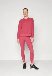 Fuksijos spalvos sportinis megztinis su apvalia iškirpte ir ilgomis rankovėmis, derinamas su atitinkančiomis tamprėmis. Juodi sportbačiai užbaigia įvaizdį.