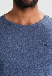 Kortärmad t-shirt med rund hals i melerad blått tyg. Har en liten broderad logotyp i röd, vit och blå på vänster bröst.