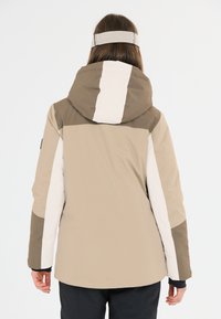 Giacca da sci beige e marrone con cappuccio, design a blocchi di colore, texture liscia e maniche aderenti. Presenta un motivo distintivo sulla cucitura posteriore.