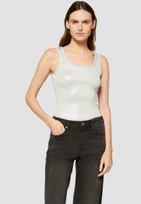Zilveren, mouwloze tanktop met een ronde hals, aansluitend ontwerp en een subtiele glans. Gecombineerd met zwarte, hooggewaiste jeans.
