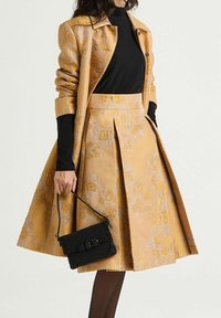 Ensemble manteau et jupe à motifs floraux jaunes avec plis, accompagné d'une pochette noire. La tenue présente un tissu texturé et une coupe sur mesure.