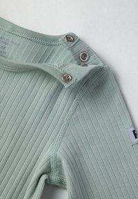 Vihreä ribbikankainen bodysuit, jossa on hopeiset nepparit olkapäällä ja "Polo"-merkki. Tasainen pinta, jossa on hienoja viivoja.