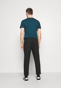 Donkerblauwe katoenen t-shirt voor mannen, korte mouwen, gecombineerd met zwarte slim-fit broek en zwarte sportsneakers met witte accenten.