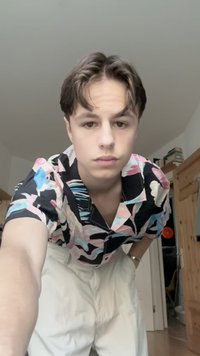 Camicia a maniche corte con sfondo nero e motivi floreali astratti colorati. Indossata con pantaloni bianchi ampi.