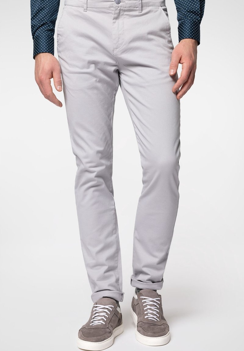 Světlé šedé chinos s úzkým střihem, s hladkým povrchem, standardními kapsami a zapínáním na knoflík, doplněné šedými teniskami.
