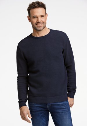 Suéter de punto azul marino con patrón texturizado, cuello redondo y puños acanalados. Combinado con jeans azules. Tejido suave, ajuste casual.