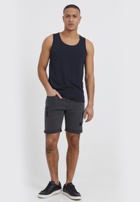 Marineblauwe tanktop, grijze denimshorts met opgerolde pijpen en zwarte sneakers. Opvallende details zijn scheuren in de shorts en een tatoeage op het been.