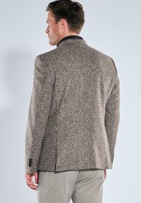 Brauner karierter Blazer mit Reverskragen, strukturierter Stoff, seitliche Schlitze und ärmellose Manschetten, Rückansicht.
