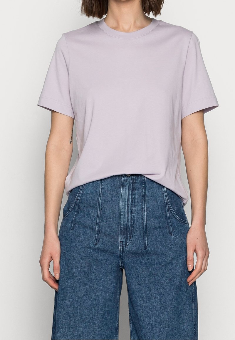 Helles lila Baumwoll-T-Shirt mit rundem Halsausschnitt und kurzen Ärmeln, kombiniert mit hoch taillierten, weit geschnittenen Denim-Hosen.