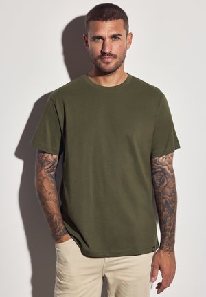 Camiseta de algodón verde oliva con cuello redondo, mangas cortas y un corte relajado, que presenta una textura sutil y sin patrones visibles.