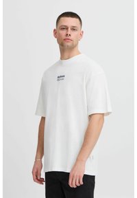 Hvit oversized t-skjorte laget av bomull, med korte ermer og rund hals. Sentral marineblå tekst sier "Handlinger Beslutninger."